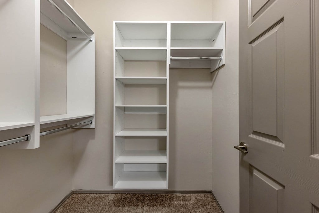 a walk in closet with white shelves and
